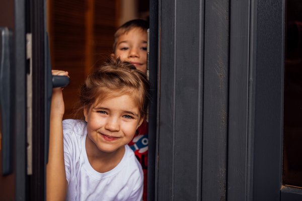 Nahaufnahme von Kindern, die aus der Tür gucken. Kleiner Bruder und kleine Schwester öffnen die Haustür. 