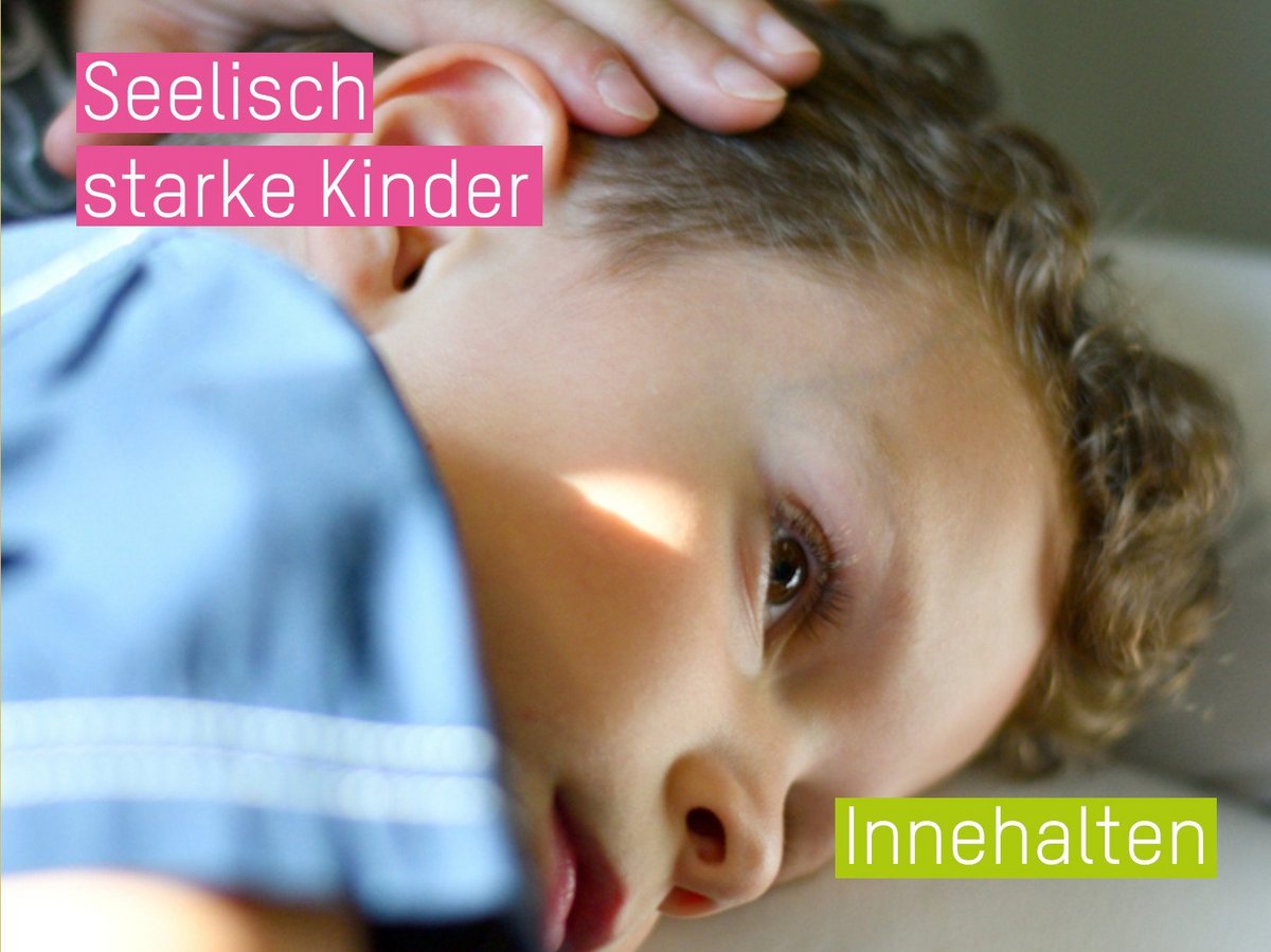 Kind, das auf dem Bauch liegt und entspannt ins Leere schaut. Eine erwachsene Hand ruht sanft auf dem Kopf.